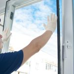 master in protective gloves, changing a double-glazed window in a plastic window, side view, against the blue sky